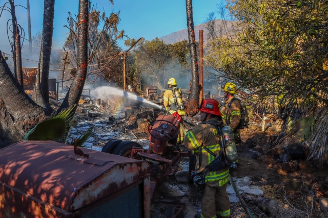 On Monday, October 16th, 2023, at 2:47 p.m., Fillmore City Fire Dept. and Ventura County & City Fire Depts. were dispatched to a reported structure fire in the 1800 block of Grand Avenue, unincorporated area west of Fillmore. The one-story cinder-block home was fully engulfed when crews arrived. The location of the home, surrounded by orchards, presented fire crews with the challenge of difficult access. Several trees and farm equipment near the home were also scorched. Additionally, downed power lines caused concern, along with the collapsing roof and side walls of the home. There was a fire hydrant nearby and Fillmore Fire Chief Keith Gurrola stated they were able to knock down the main fire “pretty fast” with the number of agencies on-scene. “But there was a lot of exterior storage that the fire had already spread into, so it was taking a lot of time to put out that fire,” said Gurrola. The owner of the home was present at the time of the fire but was not inside the structure when it started. It is not clear whether the downed power lines had fallen as a result of the fire or had been on the ground beforehand. The structure and the majority of its contents appeared to be a total loss. No one was injured. Cause of the fire is under investigation and its starting point and cost of damage are yet to be determined. Photo credit Angel Esquivel-AE News. 