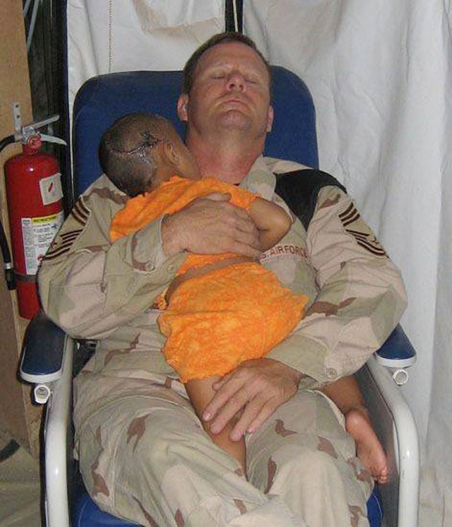 Chief Master Sgt. John Gebhardt holding an injured Iraqi child. The young infant had received extensive gunshot injuries to her head when insurgents attacked her family killing both of her parents and many of her siblings.