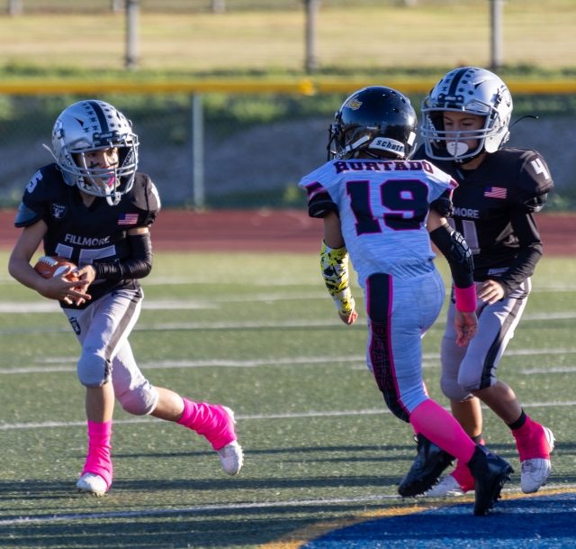 Raiders Mighty Mite’s Black #15 carrying the ball as he tries to make his way past a North Valley defense while Raiders #4 tries making the block. Photo credit Crystal Gurrola.