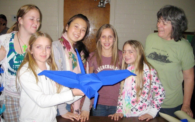 A giant origami crane is proudly displayed by Claire Faith, Sara Beylik, Nanako Matsumoto, Sonya Gonzales, Chloe Stines, and Janine Rees.