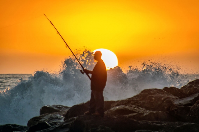 Photo of the Week "Angler on jetty at sunset, mindless of the smashing waves" by Bob Crum. Photo data: Canon 7DMKII camera, manual mode, ISO 500, Tamron 16-300mm lens @300mm, aperture f/6.3, shutter speed 1/500 of a second.