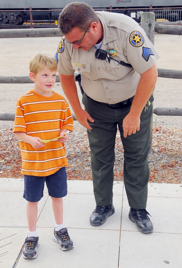 Ryan Furness (left), age 6 “and a half”, was encouraged to consider a career in law enforcement by Sgt. Dave Wareham, last week in Fillmore. The rest of the day, Ryan proudly wore the Junior Deputy badge Sgt. Wareham gave him.