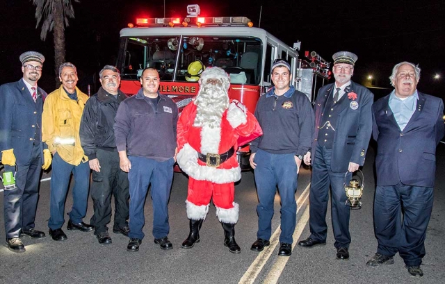 (l-r) Train Conductor Ryan Stern, Captain Al Huerta, Chief Gurrola, Firefighter Salazar, Santa, Firefighter Lechnar, Steve Phares, and Dave Wilkinson gather to take a photo with Santa. Traveling all the way from the North Pole, Santa arrives in Fillmore on the Fillmore & Western Railway Santa Train. And just in time for ole St. Nick to join the fantabulous Lions Club Christmas Parade Saturday, 12/3/16 at 1 p.m. Photo by Bob Crum.
