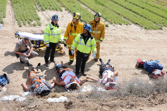 Three victims wait to be transported at the base of a 10-foot ravine. The vehicle they were riding in went down the ravine and came to rest at the edge of a crop field.