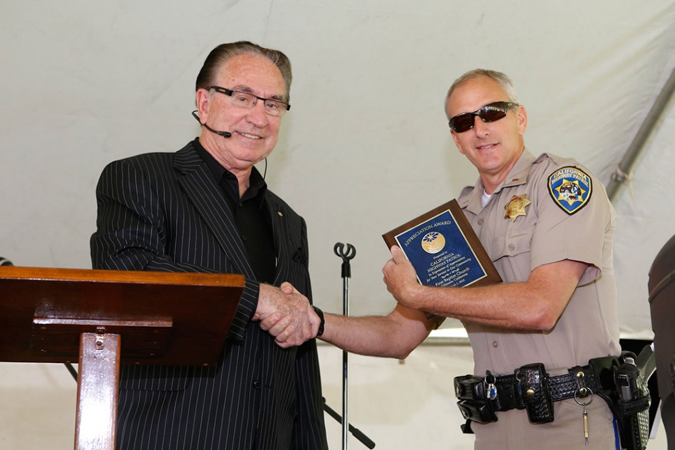 A CHP officer, representing the agency, is thanked by Pastor Golden with an appreciation plaque.