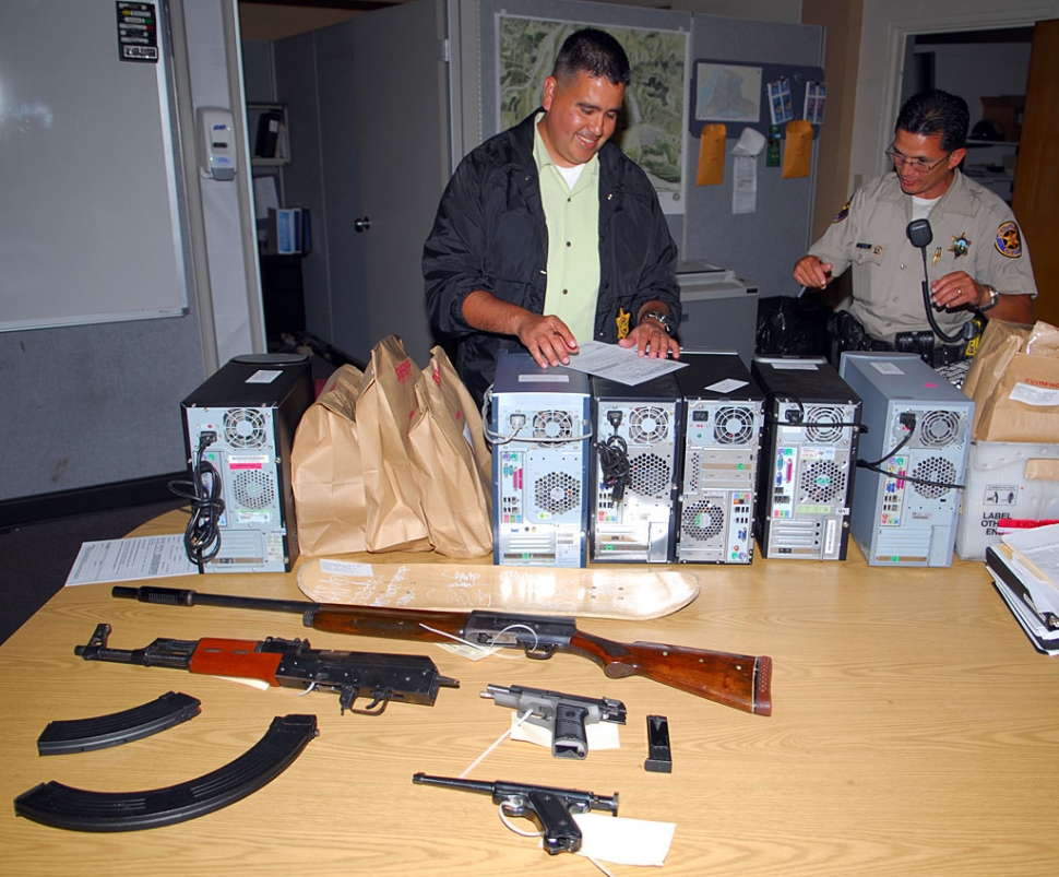 Fillmore Police Tagging Investigator Gene Torres, left, inspects the guns, ammunition, computers and other stolen property confi scated during a recent search warrant and probation searches at 7 city locations. Deputy Torres directed a 50-offi cer task force comprised of Fillmore Police and Ventura County Sheriff Deputies. Computers and cell phones taken from the residents of the arrestees will be searched for additional information.