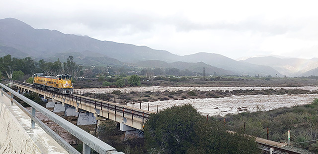 This photo was taken on January 5, 2023, the day before the railway bridge fell at Old Telegraph Road and C Street. Fillmore resident Christopher Reilley took the photo. “It rained even harder that night. It [the train] was blaring its horns so we came down to the tracks to see, maybe he detected it was about to fall. We live nearby and could see the river getting larger and larger. Eventually the split in the river became one by the bridge.” Photo credit Christopher Reilley. Inset is the collapsed railway tracks taken shortly after Mr. Reilley captured the last train to cross over Sespe Creek. Inset photo credit Angel Esquivel.