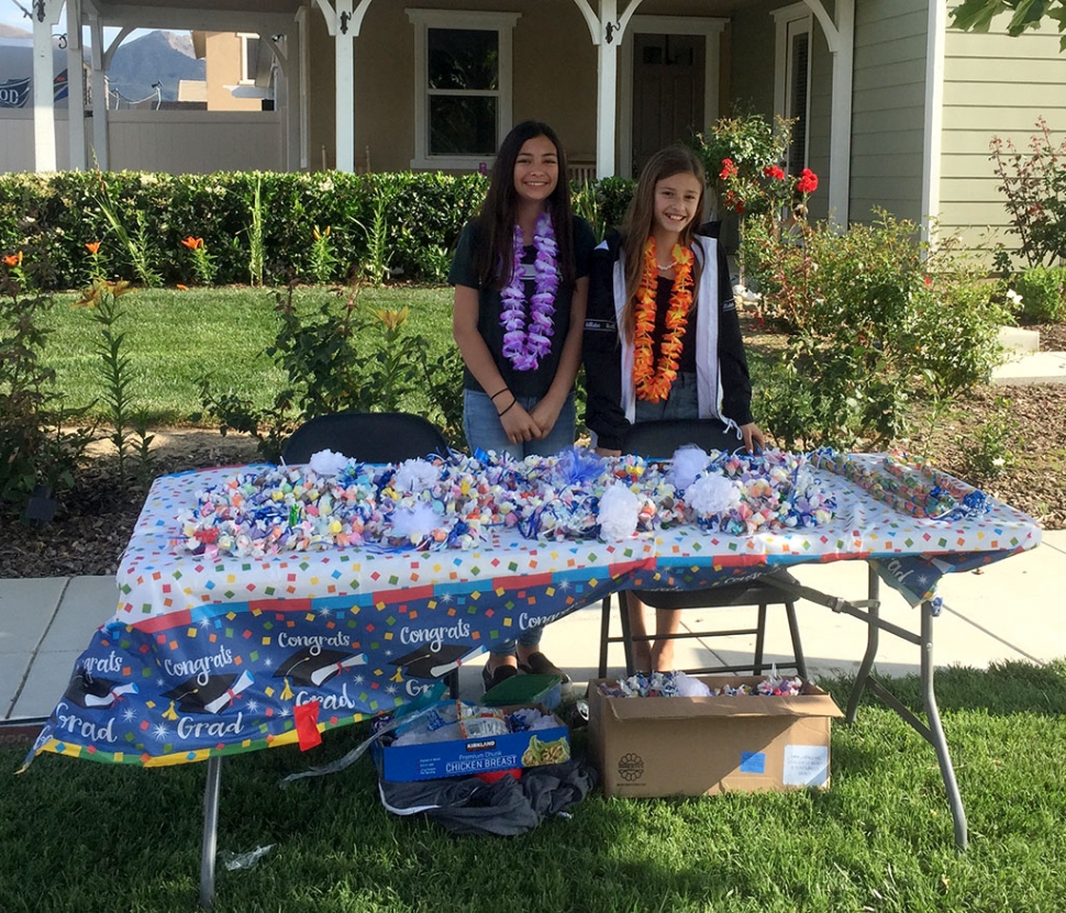 Aerin and Ashlee (l-r) are shown helping raise money for their sisters’ Flashes Cheer, by selling 2019 graduation leis at the corner of River and Mountain View. Photo courtesy Katrionna Furness.
