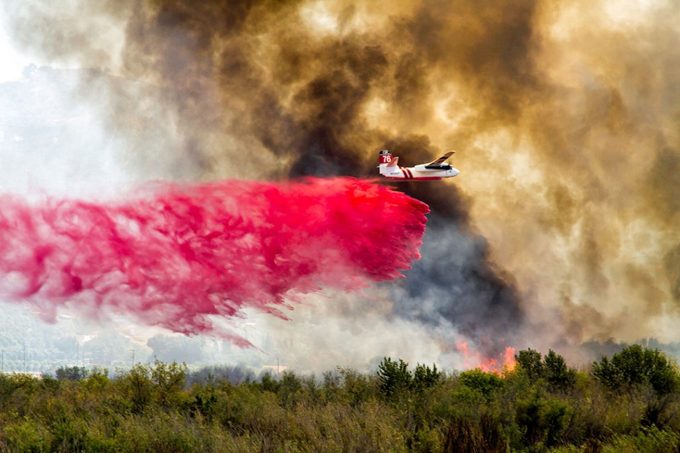 Ventura County Firefighters battled a wind-driven blaze in the Santa Clara River bottom, Monday, June 22nd, starting at 1pm. The human-caused fire started at the most southerly end of Peck Road and quickly advanced to 12th street, Santa Paula. Highway 126 remained open but off ramps at Peck, Palm and 10th Street were closed, reopening Monday night. South Mountain Road was closed between the 12th Street Bridge and Balcom Canyon. A voluntary evacuation notice was issued but later lifted. As of press time approximately 164 acres had burned, and the fire was 80% contained. Air crews could be seen dropping flame retardant on the fire, above. Photo courtesy Bob Crum.