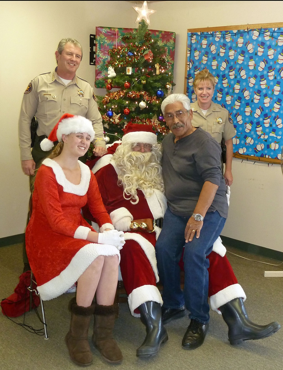 Christmas at he Fillmore Police Storefront Tuesday brought out the child in all who were there. Pictured (standing left) is Sheriff Geoff Dean, Santa and his helper, Community Resource Officer Max Pina, and Fillmore Capt. Monica McGrath.