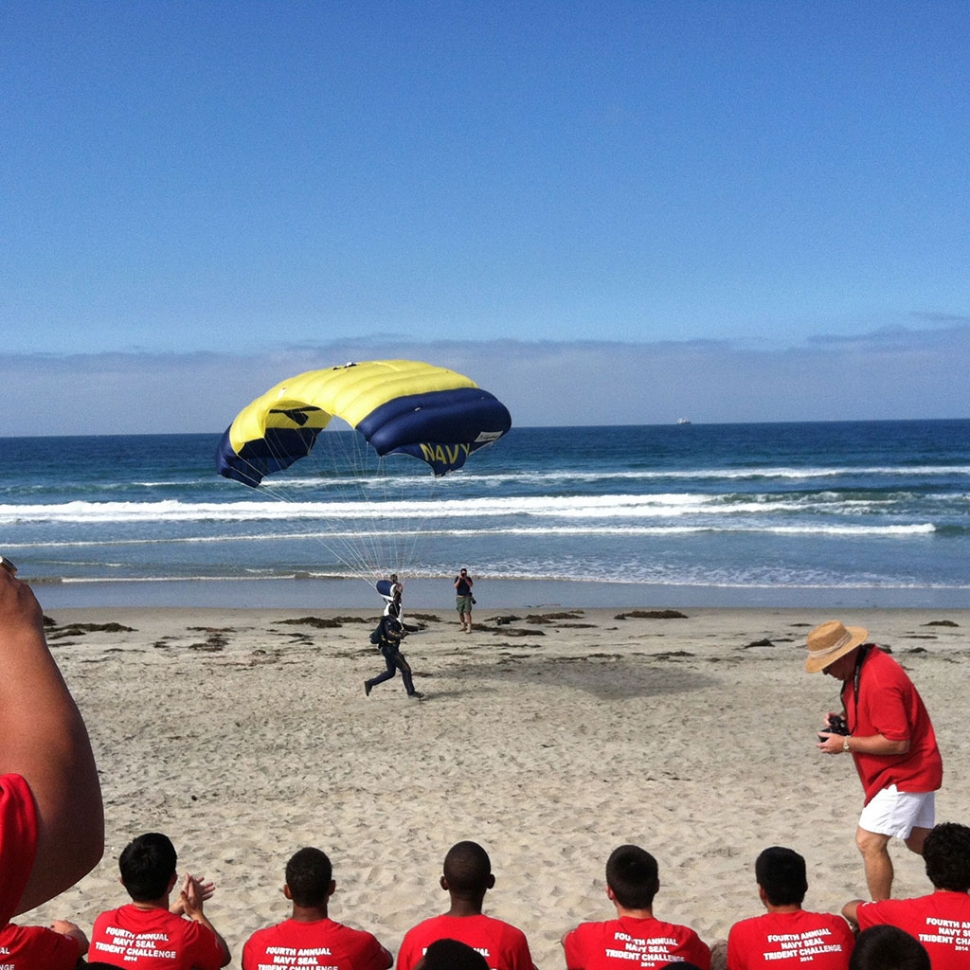 Athletes from 13 high schools participated in the Fourth Annual Navy SEAL Invitational at the Naval Special Warfare Center May 10th, 2014. The 13 high schools each brought teams of 7 athletes (plus one alternate) to compete in a race comprised of Navy SEAL physical training techniques. Right, the student athletes watch as a Navy SEAL Parachutes onto the beach.